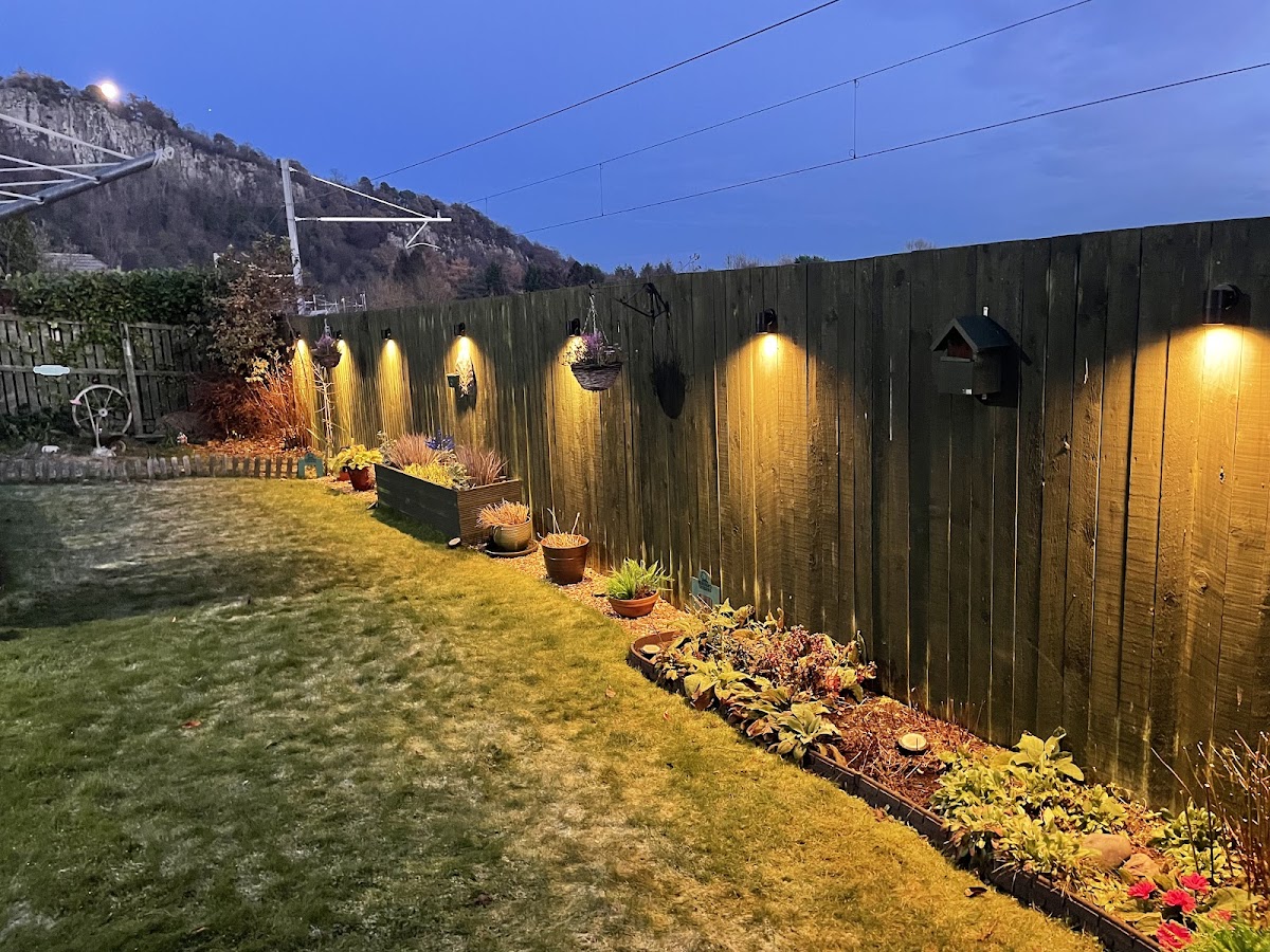 Garden lighting at dusk with fence-mounted spot lights