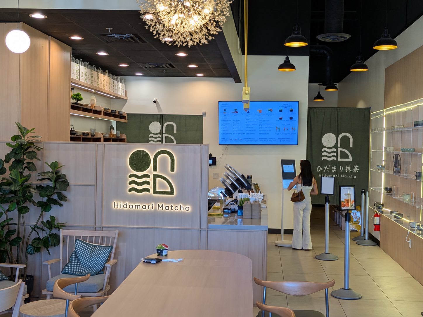 The counter at Hidamari Matcha, with the logo wall and a sage noren printed ひだまり抹茶