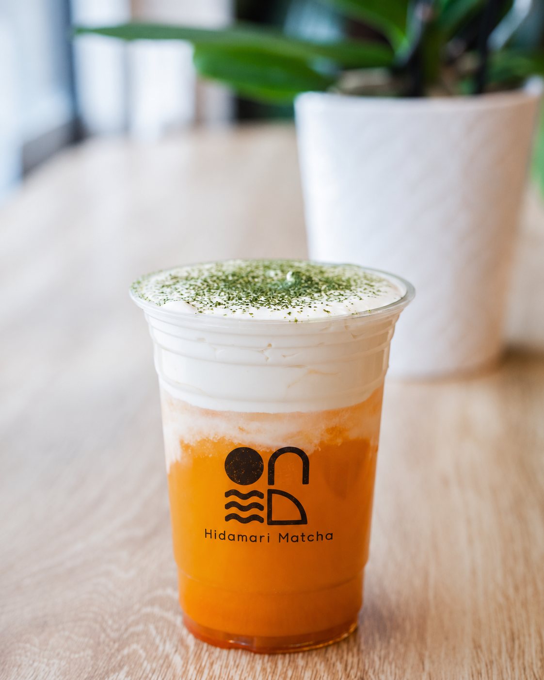 Mango Jasmine Tea Cheese Foam, bright orange tea under a thick cream topping, on a pale oak table