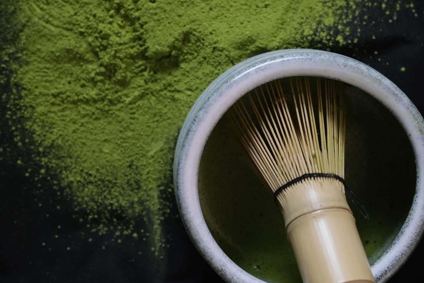 A bamboo whisk resting in a bowl of matcha, powder scattered around it